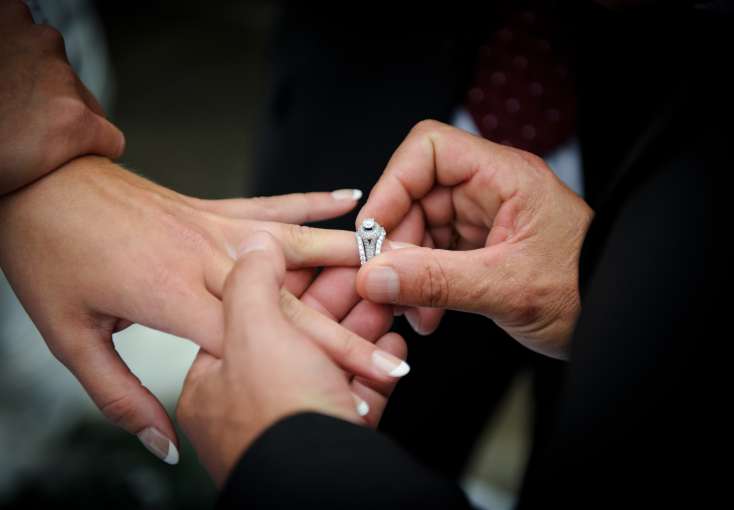 Groom placing wedding ring on bride's finger.