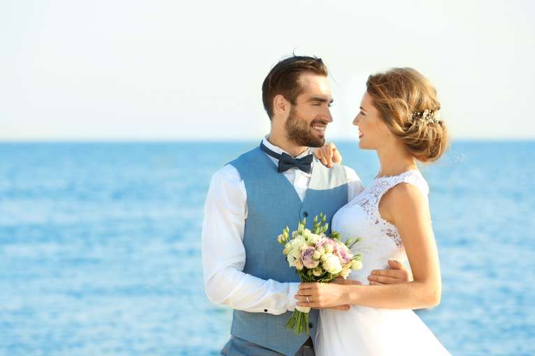 Newly married couple embracing in evening at their wedding with sea in background