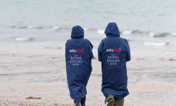 Couple walking along Falmouth beach on Autumn day wearing Royal Duchy Hotel branded dry robes