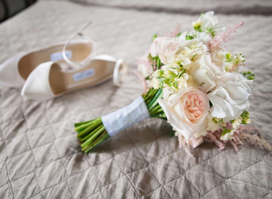 Brides bouquet and shoes placed on top of a bed