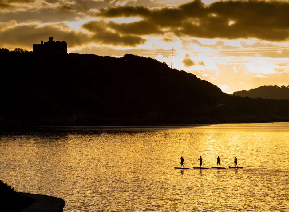 Four people standing on paddle boards at sea in Falmouth bay