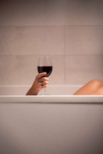 Hotel guest enjoying glass of red wine in bath